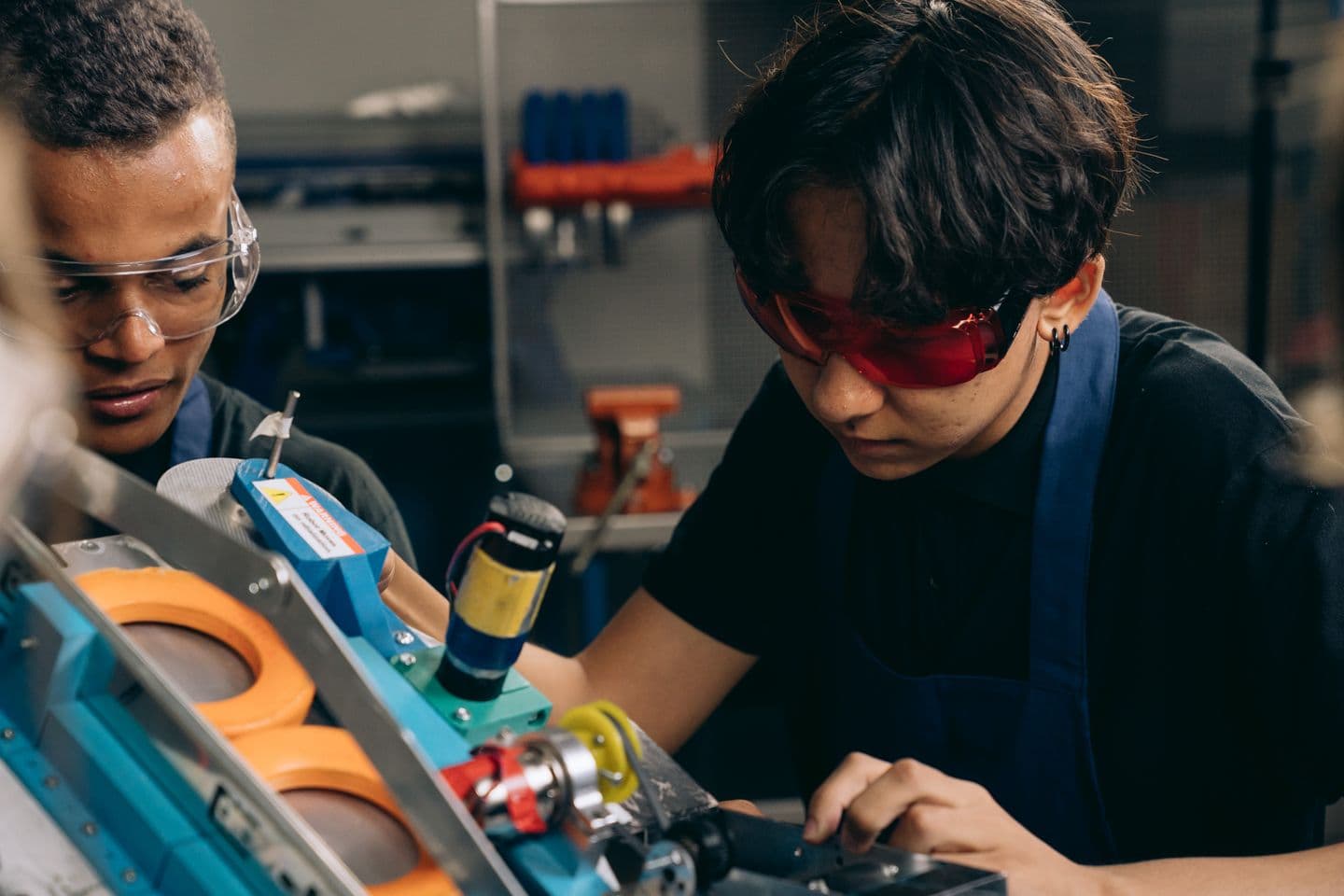 Two technicians wearing safety glasses working together on workshop equipment.