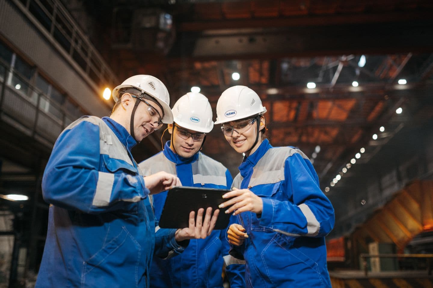 Three engineers in protective clothing reviewing a tablet in an industrial workshop.