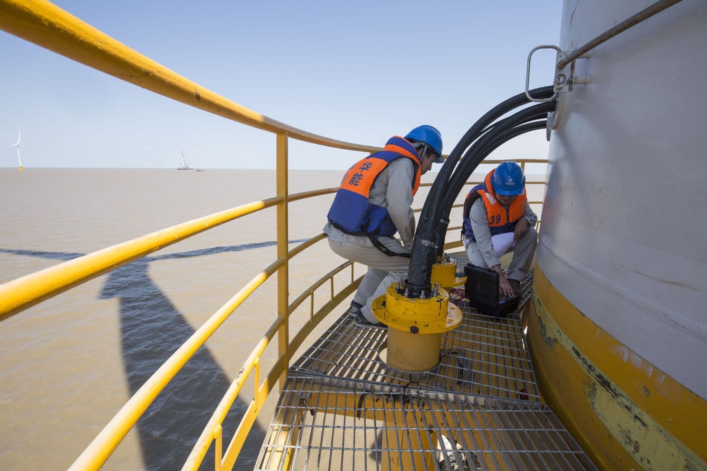 Technicians servicing equipment on an offshore wind turbine platform.