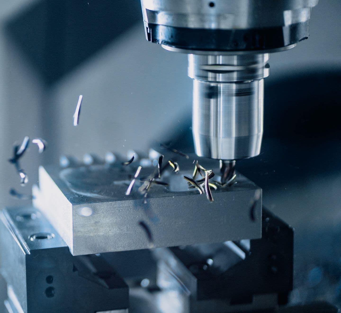 Milling tool cutting a metal component, with chips visible around the workpiece.
