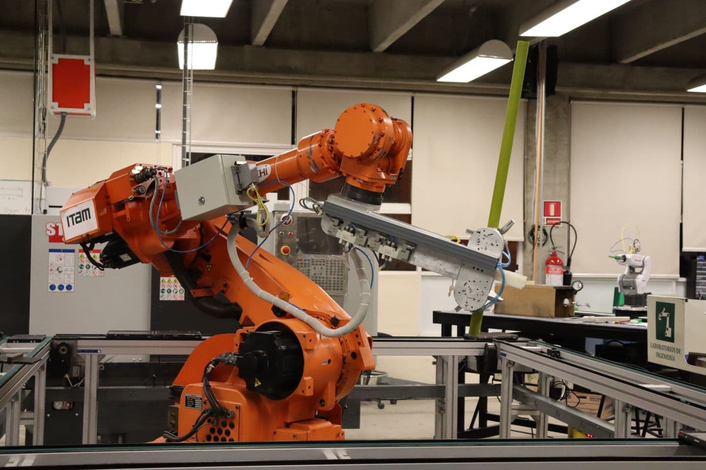 Orange industrial robot with handling tooling beside a conveyor in an automation workspace.
