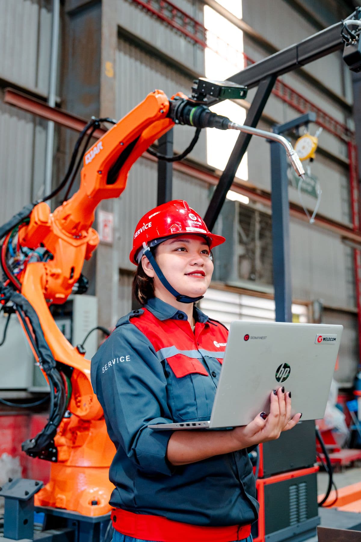 Engineer holding a laptop beside industrial robotic machinery.