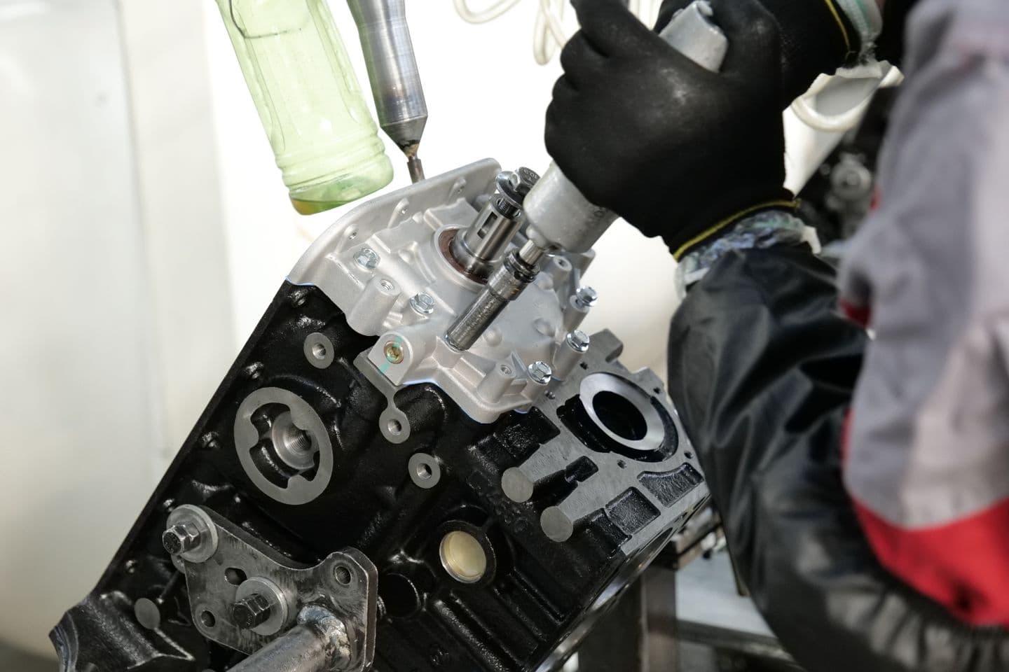Gloved technician fitting components into an automotive engine block.